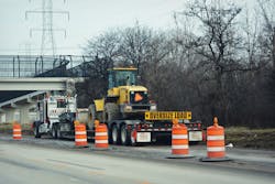 A semi truck tractor bed pulling a yellow tractor with orange construction cones by a bridge on an interstate highway in Wisconsin. A semi truck tractor bed pulling a yellow tractor with orange construction cones by a bridge on an interstate highway in Wisconsin.