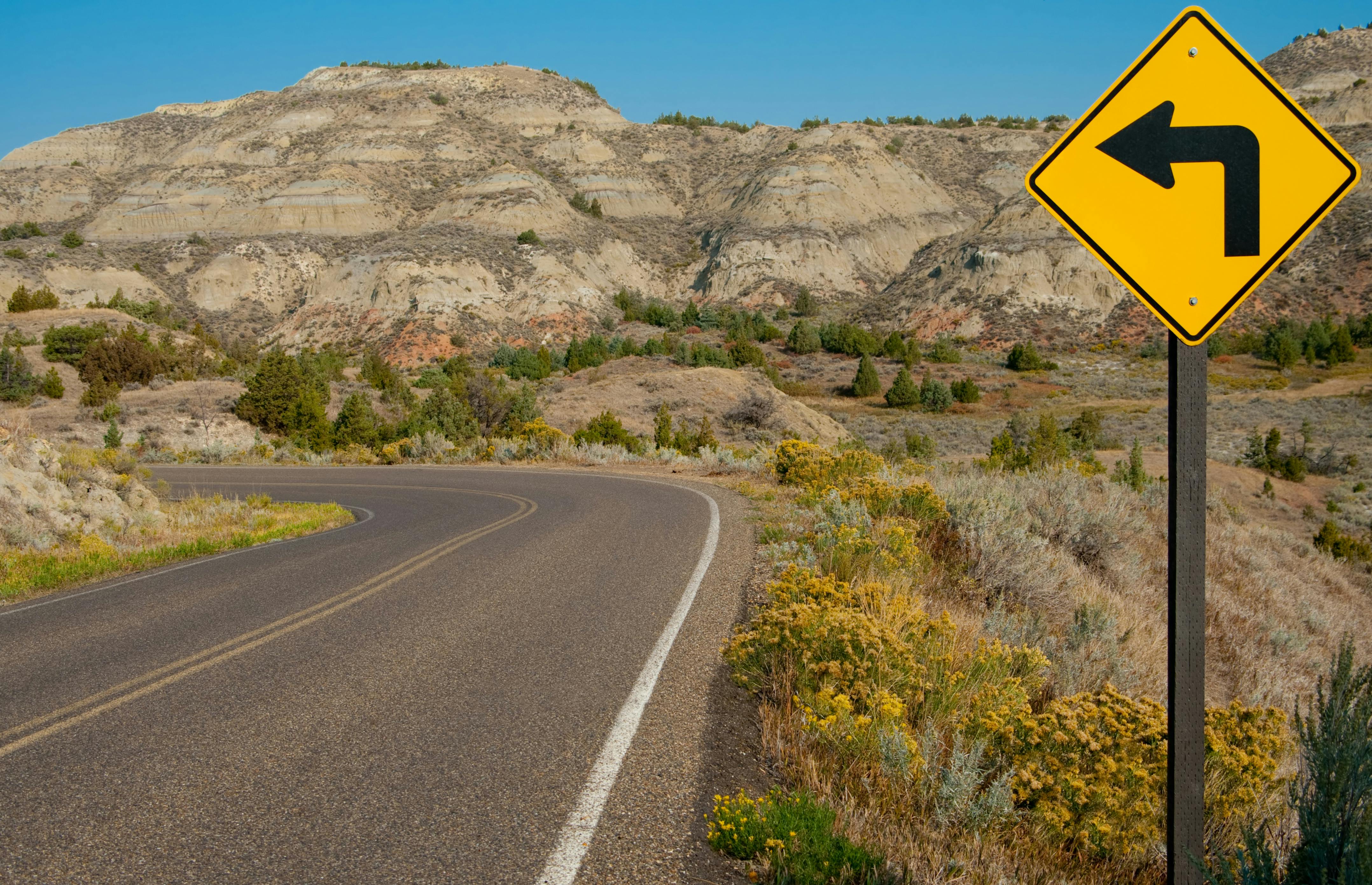 A roadway with a sharp left turn sign through Theodore Roosevelt National Park in southwest North Dakota.
