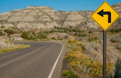 A roadway with a sharp left turn sign through Theodore Roosevelt National Park in southwest North Dakota. A roadway with a sharp left turn sign through Theodore Roosevelt National Park in southwest North Dakota.