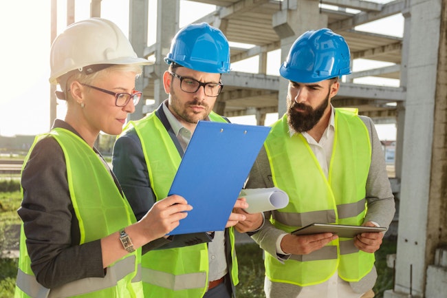 Three civil engineers looking at plans on a job site.
