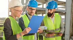 Three civil engineers looking at plans on a job site.