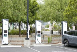 Three electric vehicle chargers and an electric vehicle being charged in a parking lot in California. Three electric vehicle chargers and an electric vehicle being charged in a parking lot in California.