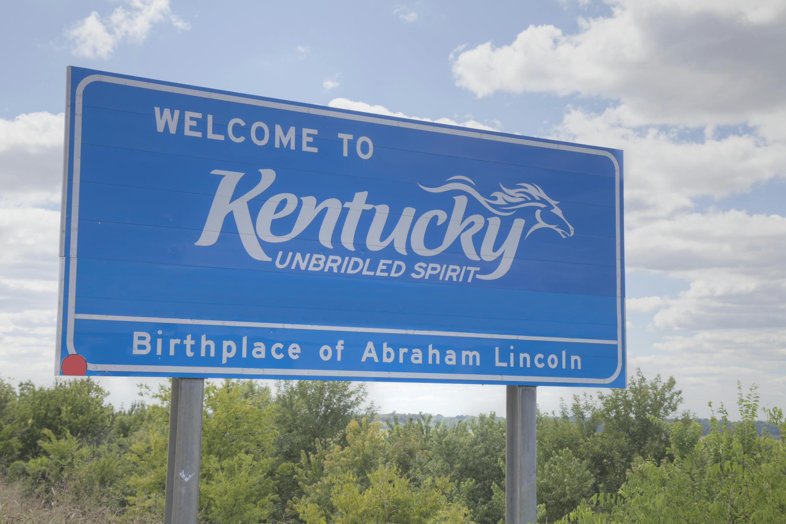 A Welcome to Kentucky sign located along the side of a highway.