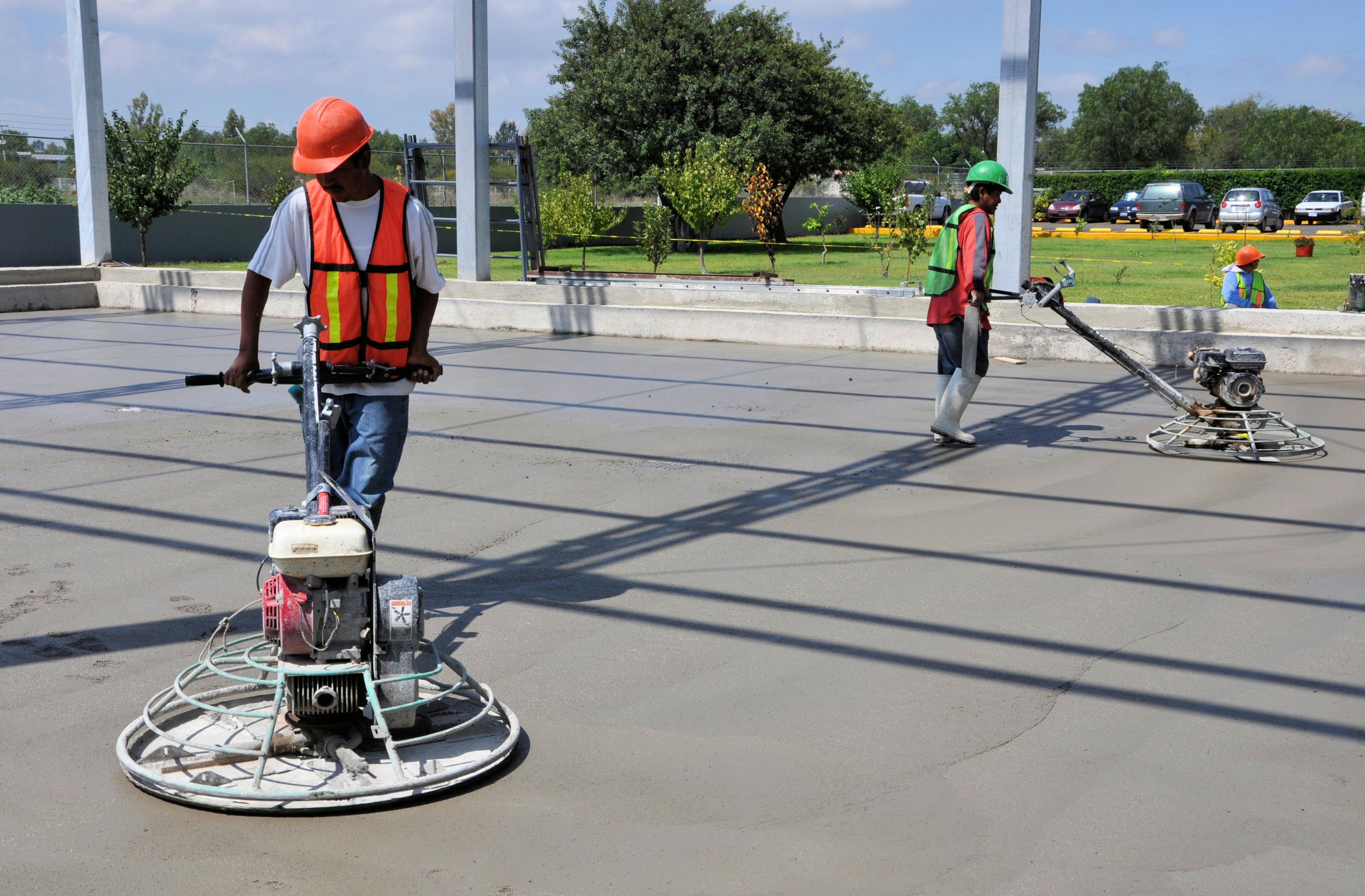 Two workers finishing a concrete floor with a smoothing machine.