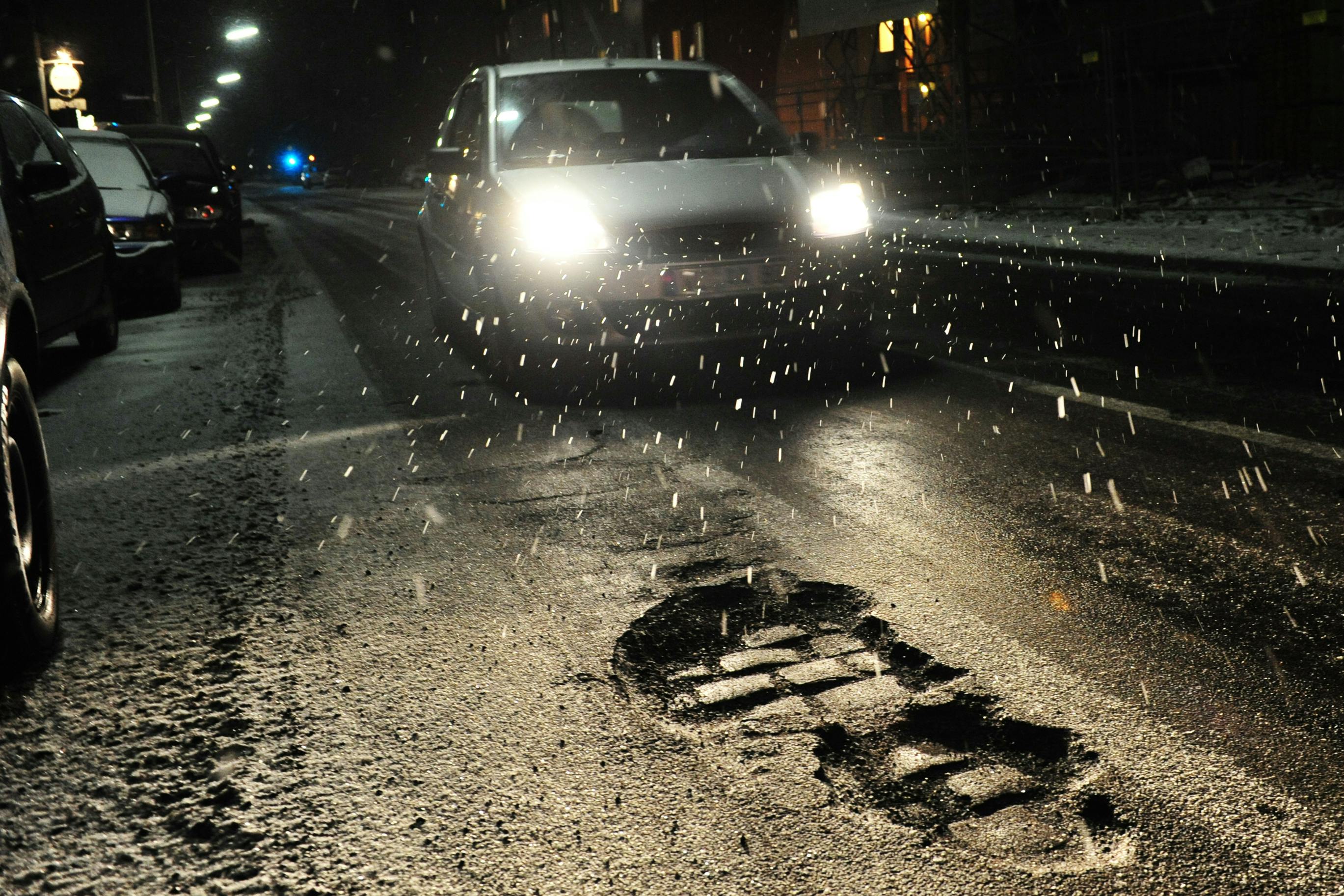 A car is driving towards a large pothole at night.