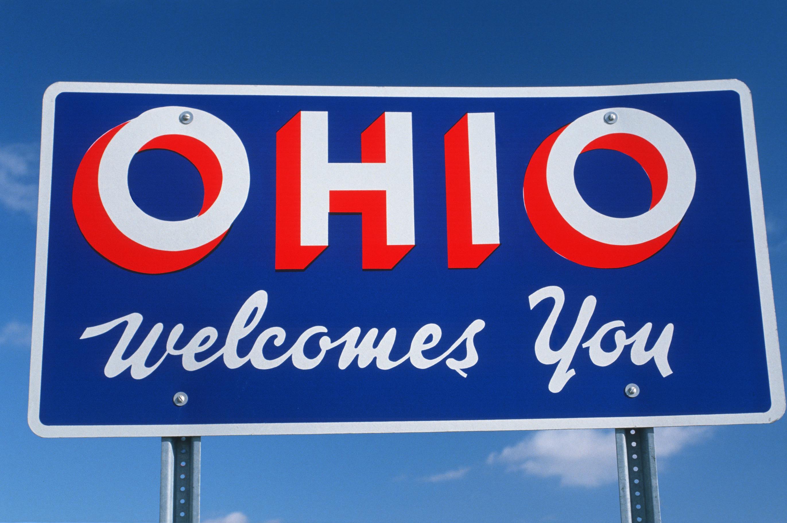 An Ohio Welcomes You sign against the skyline along the side of a highway.