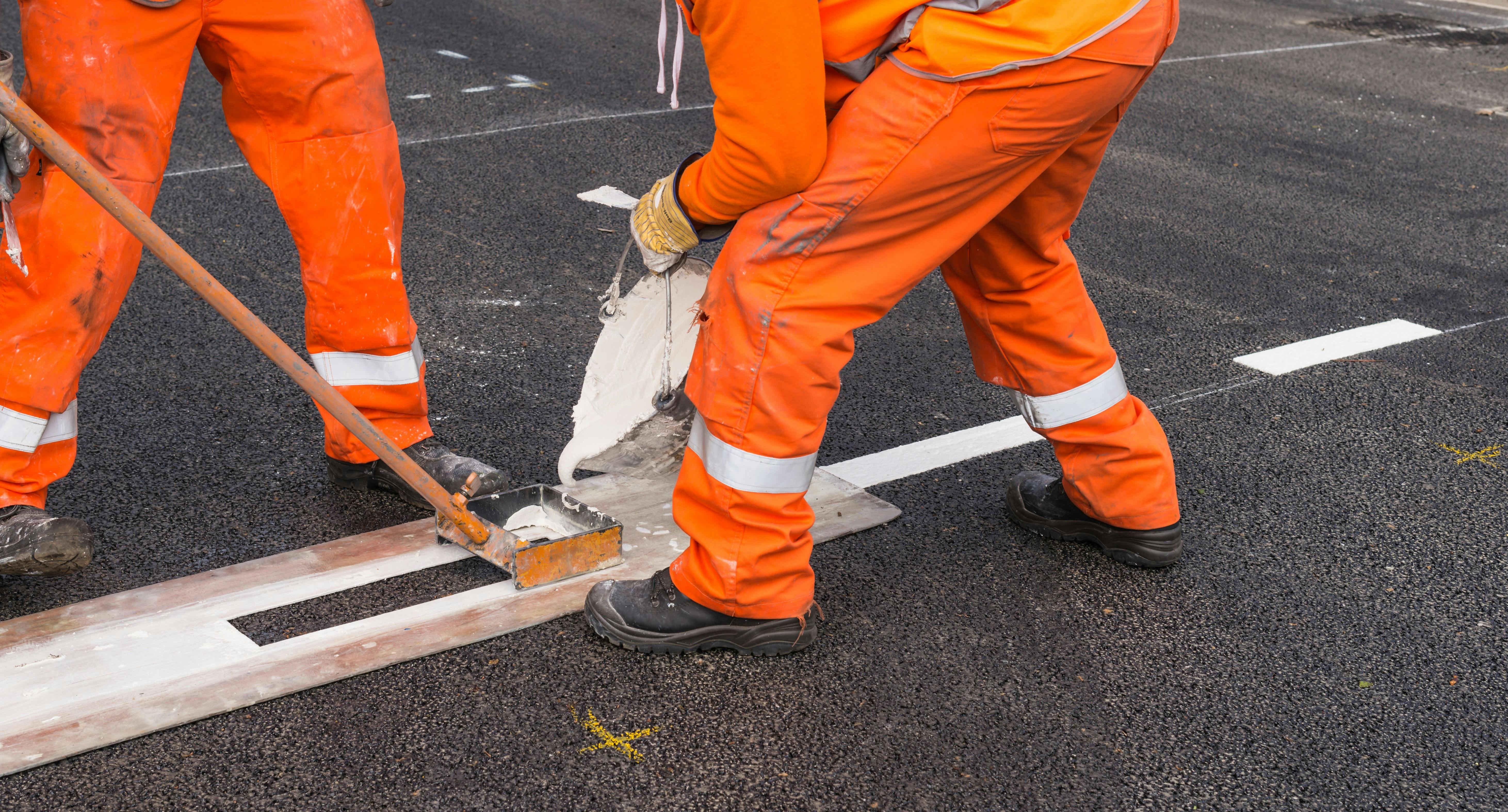 Construction crews painting lane striping on a roadway.