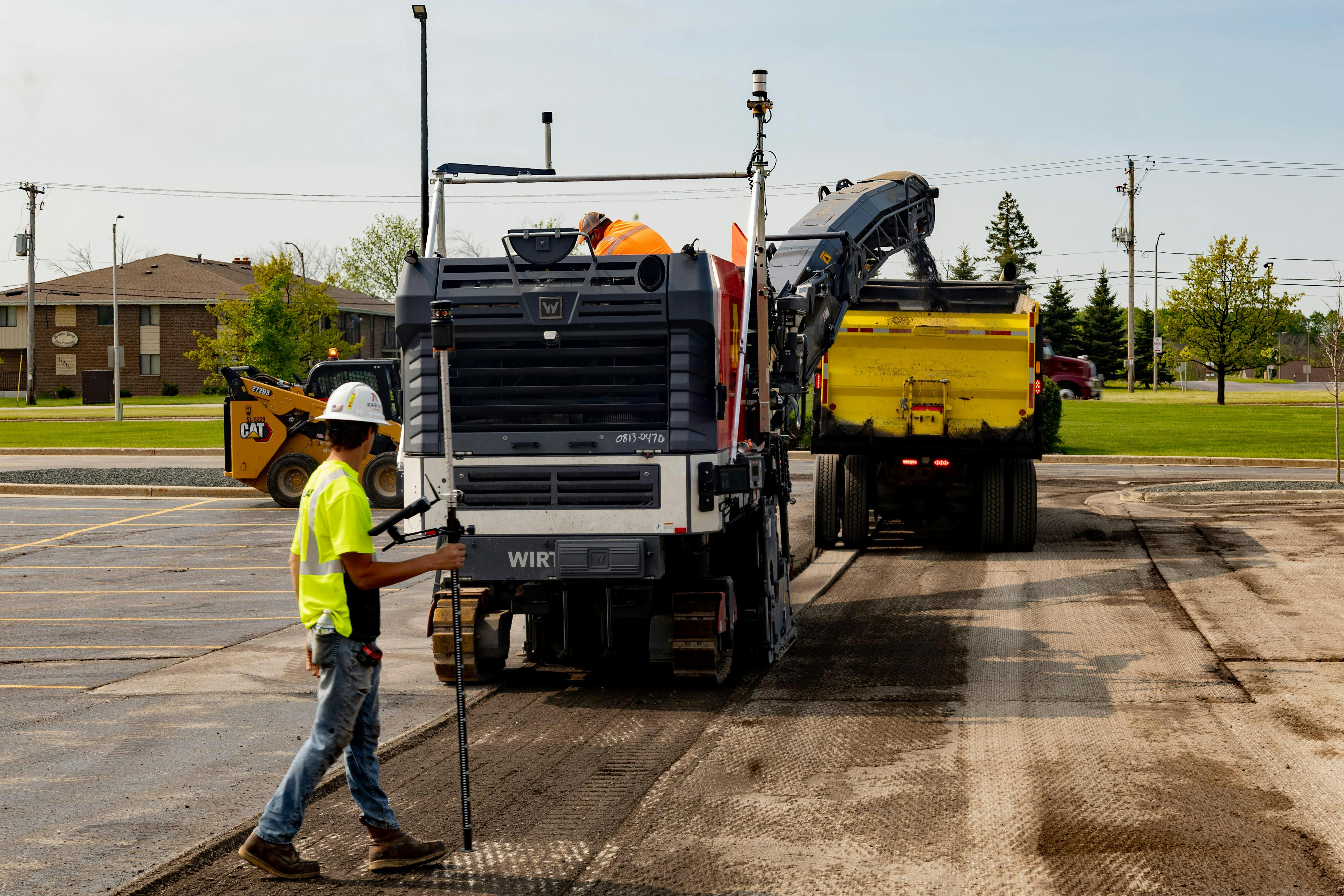 Trucks milling asphalt in a parking lot.