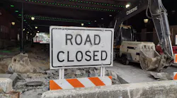 A road closed sign outside of a construction site in an urban area.