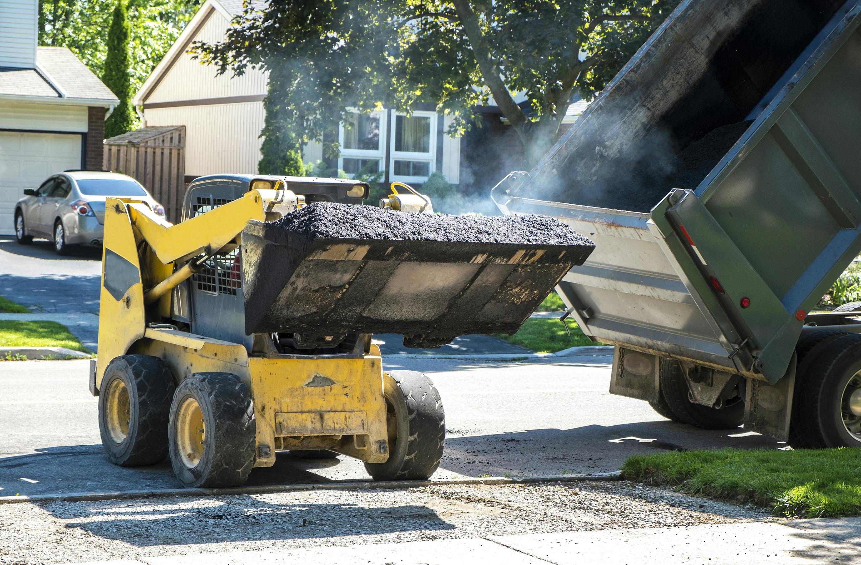 A large truck transferring asphalt into a smaller truck.