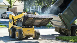 A large truck transferring asphalt into a smaller truck.