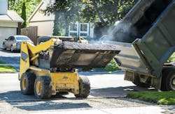 A large truck transferring asphalt into a smaller truck. A large truck transferring asphalt into a smaller truck.