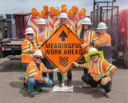 Road workers gathered around an orange construction sign stating 'Meaningful Work Ahead.' Road workers gathered around an orange construction sign stating 'Meaningful Work Ahead.'