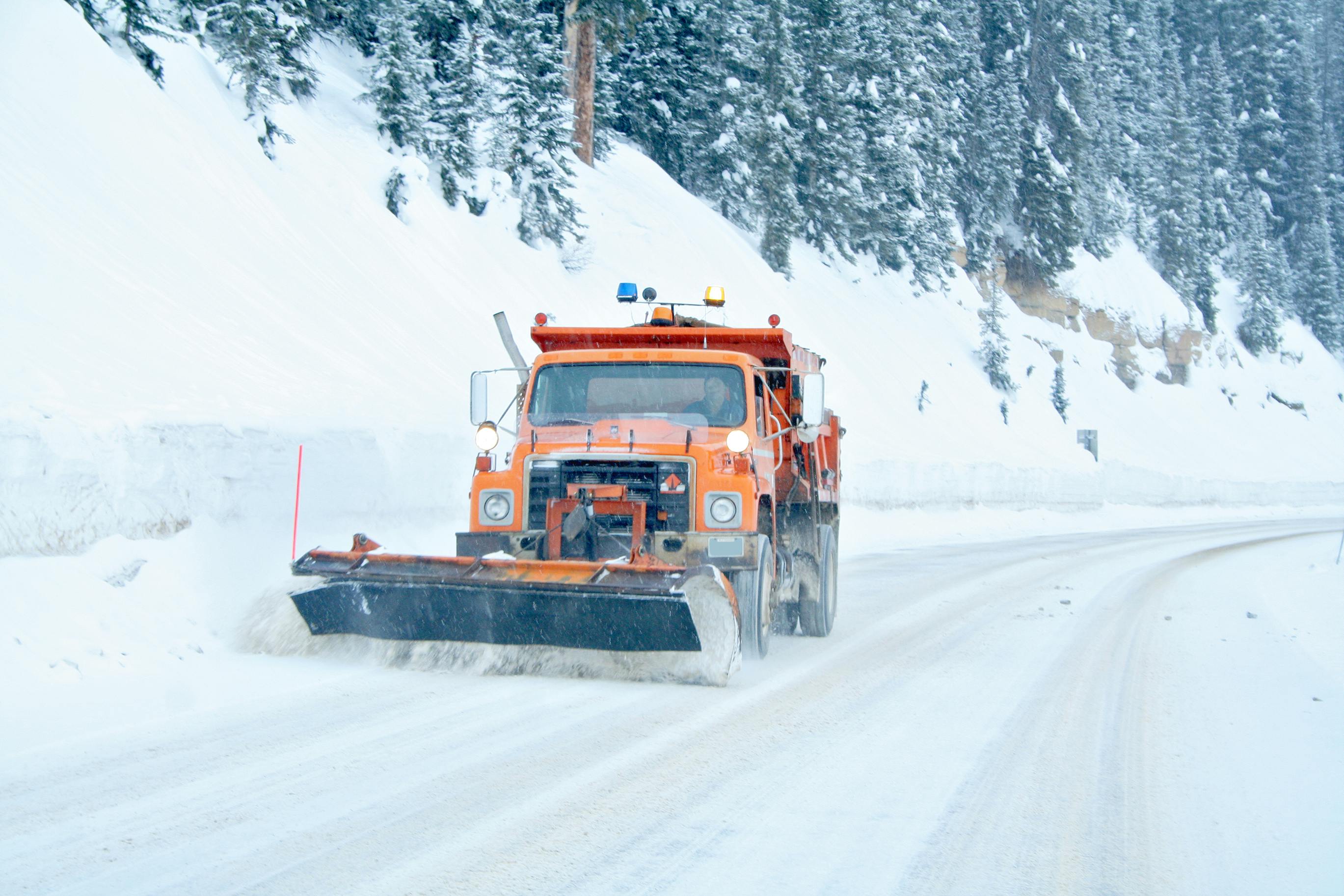 A snow plow driving down a snowy roadway.
