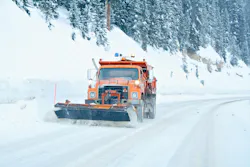 A snow plow driving down a snowy roadway. A snow plow driving down a snowy roadway.