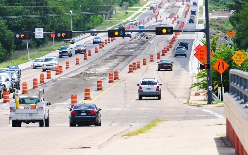 Vehicles driving past a work zone marked with cones and barrels.