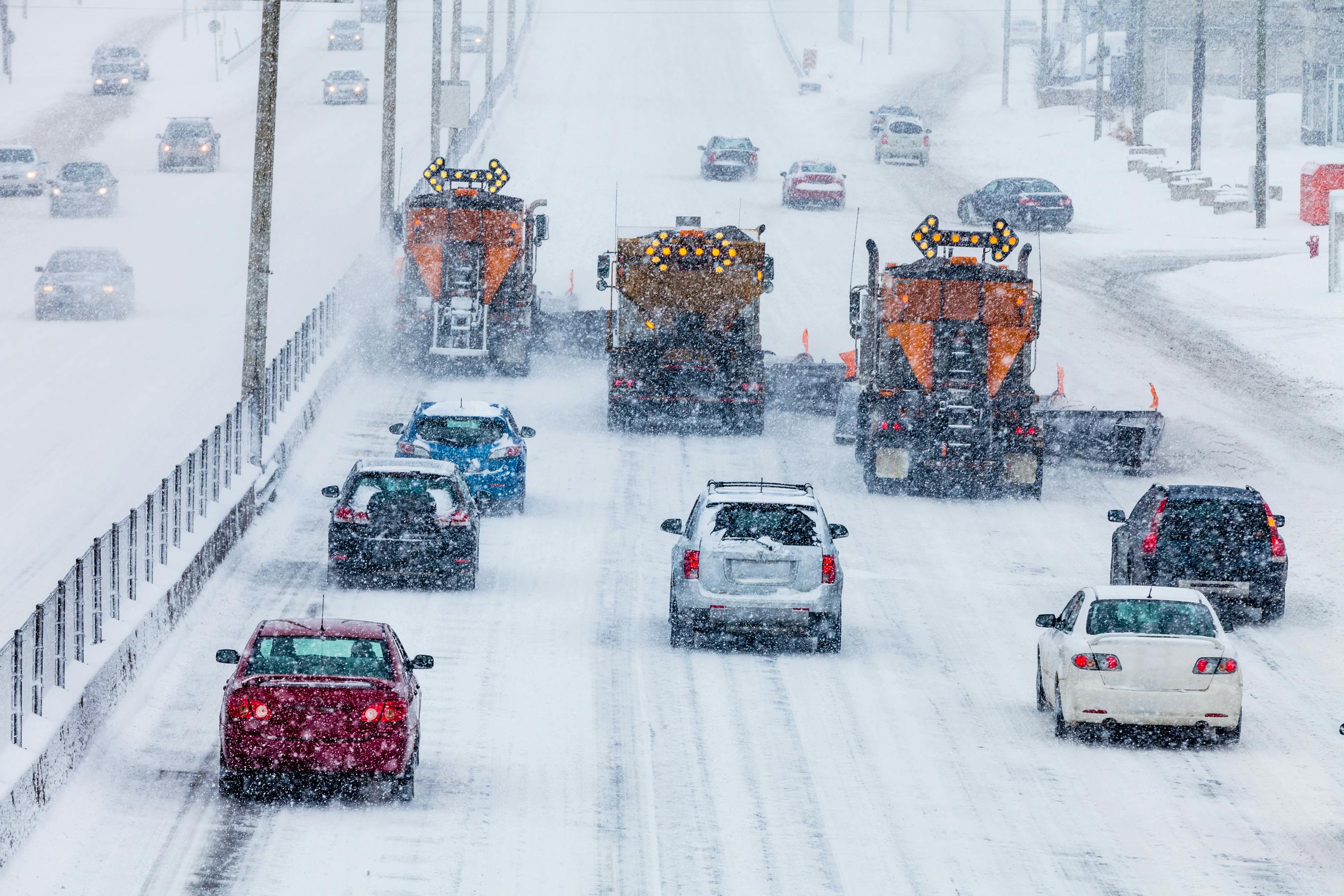 Traffic behind a fleet of plows on a snowy highway.
