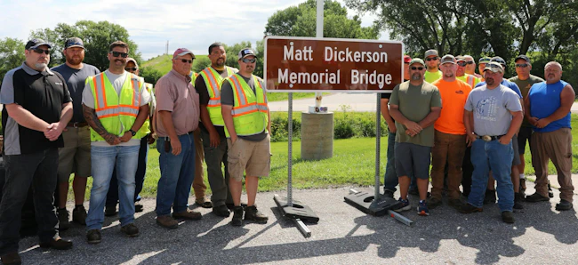 Iowa DOT District 4 staff and Matt Dickerson&rsquo;s coworkers gather around the newly unveiled Matt Dickerson Memorial Bridge sign during the dedication ceremony in Neola on June 11.