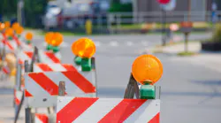 Stock photo of a row of road traffic barricades with yellow warning lights guiding vehicles through a work zone.