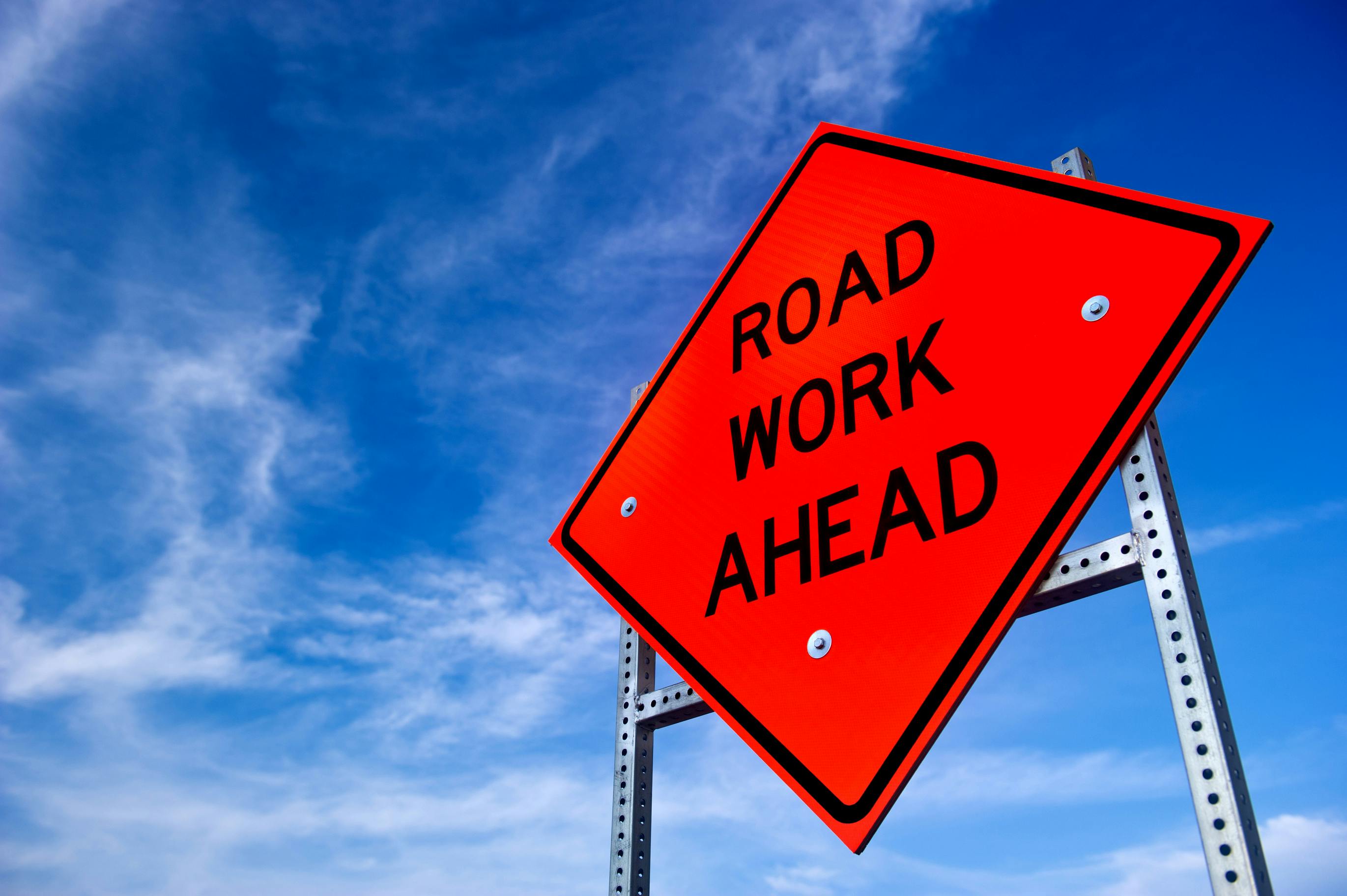 A road work ahead sign on the side of a roadway.