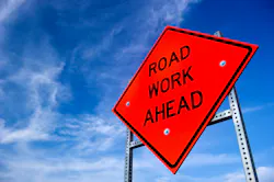 A road work ahead sign on the side of a roadway.